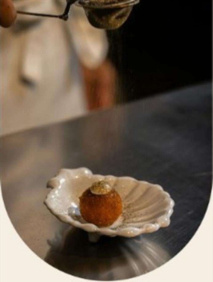 A plated dessert in a shell dish as a fine powder is dusted over it.