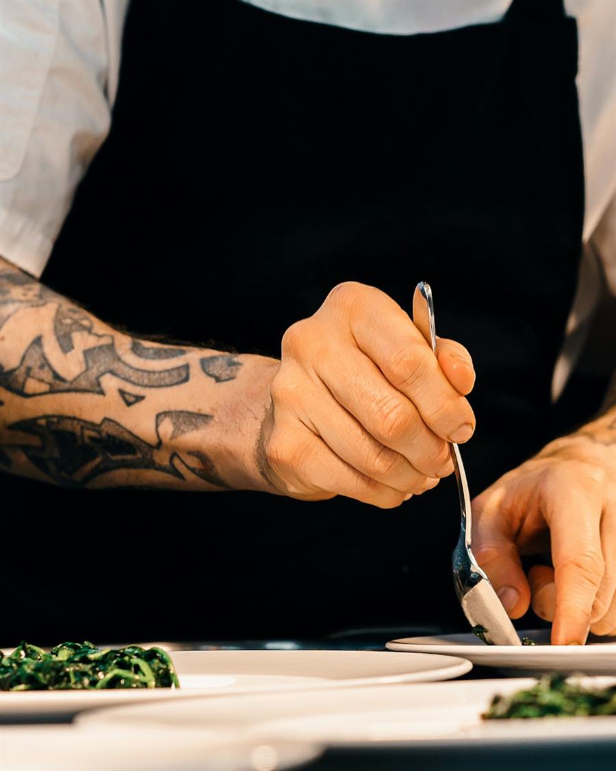 Illustrative image: a chef's hands finishing plates of greens.